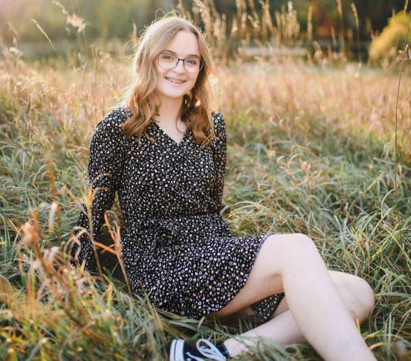 Girl smiling at camera, sitting amongst sunlit wheat grass plants